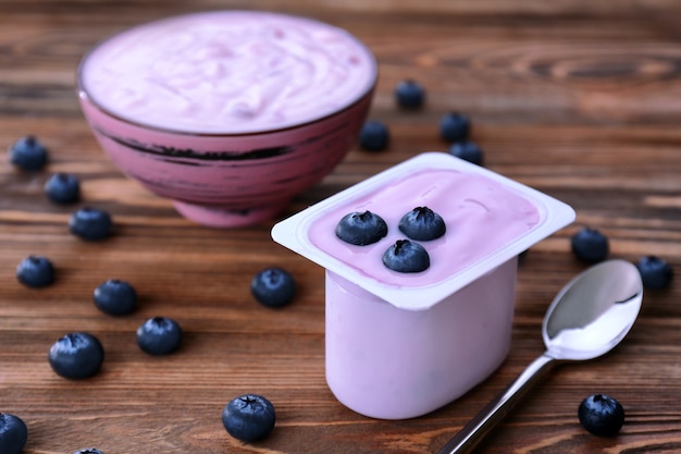 Plastikbecher mit Joghurt und Blaubeeren auf Holztisch