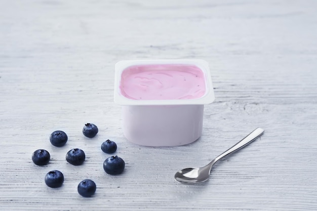 Plastikbecher mit Joghurt und Blaubeeren auf Holztisch