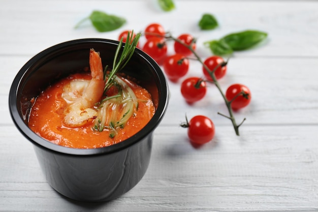 Plastikbehälter mit köstlichen Garnelen in Tomatensauce auf Holztisch