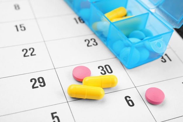 Plastikbehälter mit Pillen auf Papierkalender in Nahaufnahme