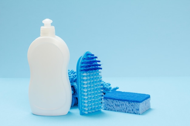 Plastikflasche mit Spülmittel, ein Lappen, ein Schwamm und eine Bürste auf blauem Hintergrund