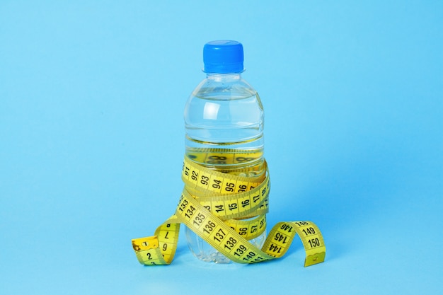 Plastikflasche mit Wasser und Maßband auf blauem Hintergrund.