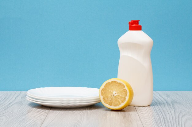 Plastikflasche Spülmittel, saubere Teller und Zitrone auf Holzbrettern und blauem Hintergrund. Wasch- und Reinigungskonzept.