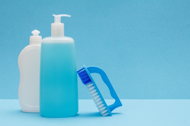 Plastikflaschen mit Spülmittel, Glasreiniger und Bürste auf blauem Hintergrund. Wasch- und Reinigungskonzept.