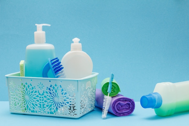 Plastikkorb, Flaschen Spülmittel, Glas- und Fliesenreiniger, Bürsten, Müllsäcke auf blauem Hintergrund. Wasch- und Reinigungskonzept.