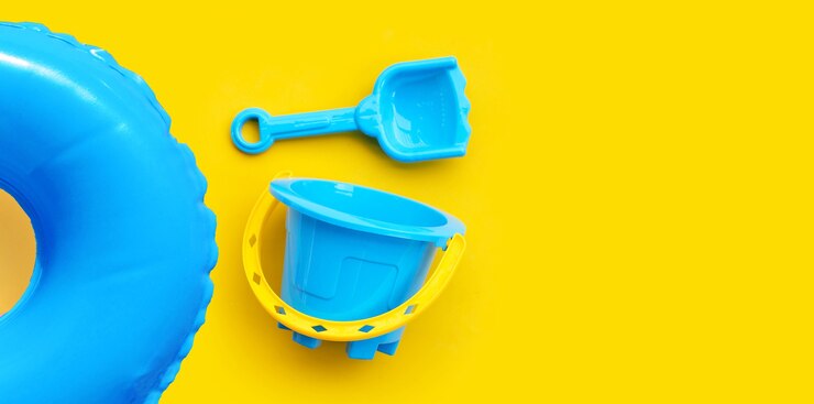 Foto plastikspielzeug, schwimmbadring mit eimer und schaufel für sand auf gelber oberfläche.