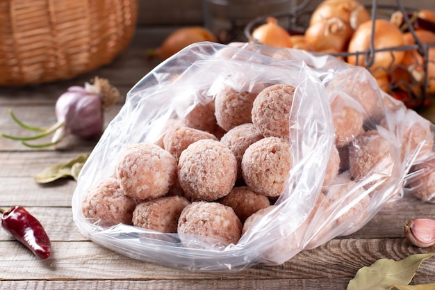 Plastiktüten mit gefrorenem Fleisch und Fleischbällchen in Plastiktüte auf einem Holztisch