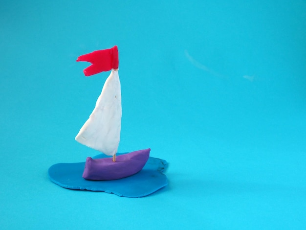 Plastilin-Schiff mit einem Segel und einer Flagge, die auf blauem Hintergrund isoliert sind