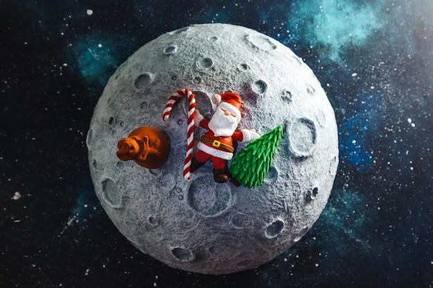 Plastilin-Weihnachtsmann liegt mit einer Tüte voller Geschenke und einem Weihnachtsbaum auf dem Mond