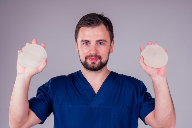 Plastischer Chirurg männlich, der vor dem weißen Hintergrund des modernen Augmentations-Implantatstudios gezeigt wird
