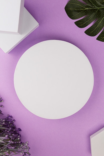 Foto plataforma blanca con formas geométricas y flores y monstera sobre fondo morado