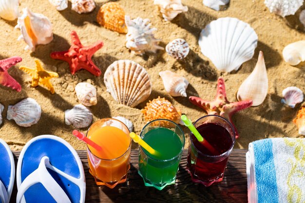 En la plataforma de madera hay sandalias de playa y una toalla y un vaso lleno de bebida fría de fruta con una pajita