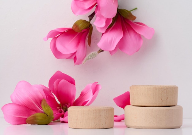 Plataforma de madera redonda vacía y ramas con flores de magnolia rosa sobre un fondo blanco Lugar para la demostración de productos cosméticos