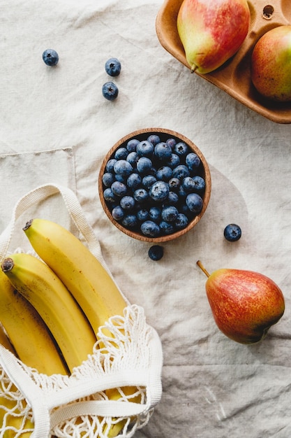 Plátanos en una bolsa de red, peras y arándanos en una servilleta de lino Fondo de alimentos ecológicos y de verano