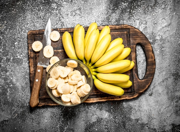 Foto plátanos frescos con trozos de plátanos en rodajas en un recipiente. sobre mesa rústica.