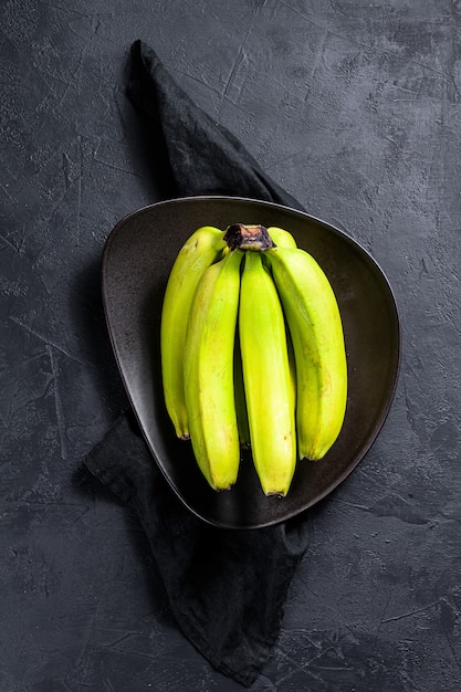 Foto plátanos verdes en un plato. fondo negro. vista superior. espacio para texto. fruta tropical