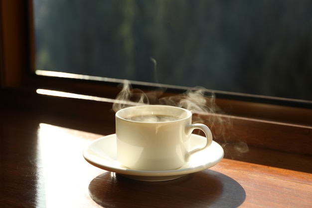 Platillo con taza de bebida caliente en el alféizar de la ventana de madera