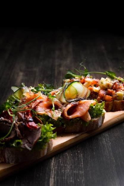 Un plato de 3 tapas diferentes rellenas de pescado de carne y varios microvegetales servidos en una tabla sobre un fondo oscuro