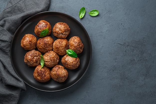 Un plato con albóndigas y albahaca sobre un fondo oscuro. Vista superior, espacio de copia.