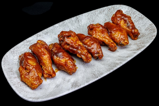 Foto plato de alitas de pollo a la barbacoa sobre fondo negro