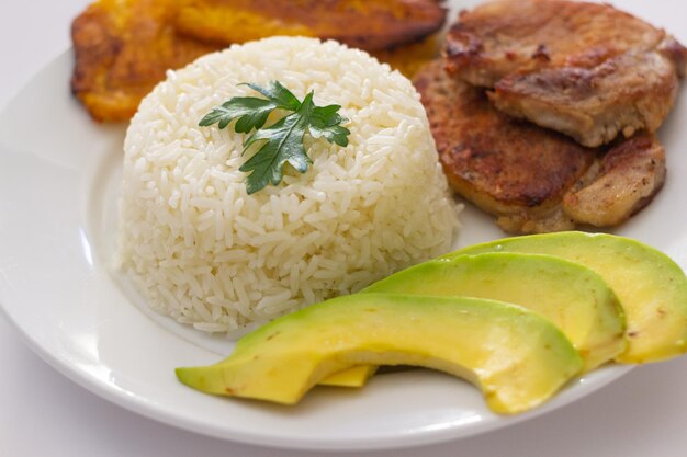 Plato almuerzo dominicano, tostones fritos, arroz blanco acompañado de varios aguacates cortados, comida en casa, toma cerrada.