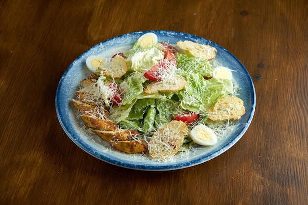 El plato americano clásico es la ensalada César con pollo, crutones, parmesano y tomates en un plato azul sobre una superficie de madera.