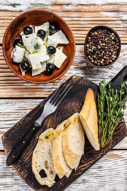 Plato de antipasti con queso feta fresco, pan y aceitunas. Mesa de madera blanca. Vista superior.