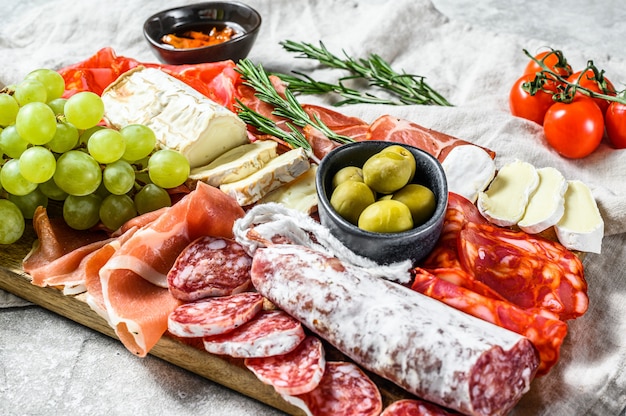 Plato de antipasto de embutidos con uvas, jamón serrano, lonchas de jamón, cecina, salami de chorizo, fuet, camembert y queso de cabra. Vista superior.