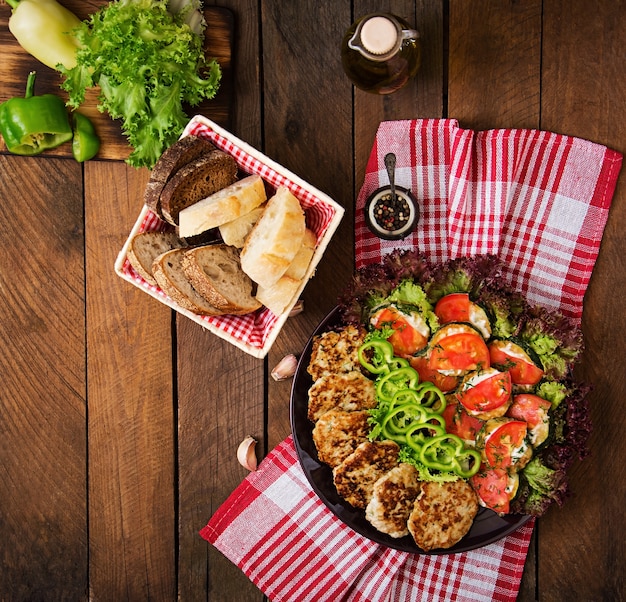 Plato con un aperitivo de calabacín frito con tomates y suculentas chuletas de pollo con calabacín.