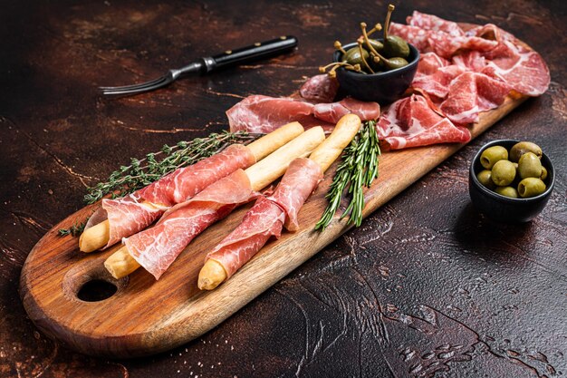 Plato de aperitivo de carne con palitos de grissini Prosciutto crudo Salami y Coppa Salchicha y aceitunas Fondo oscuro Vista superior