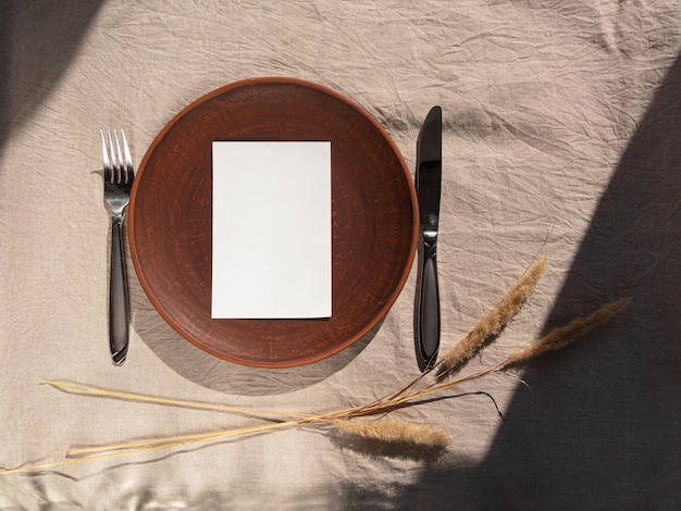 Plato de arcilla artesanal vacío hecho a mano con tenedor cuchillo sobre mantel Lugar de mesa plato hecho a mano Decoración interior natural del hogar