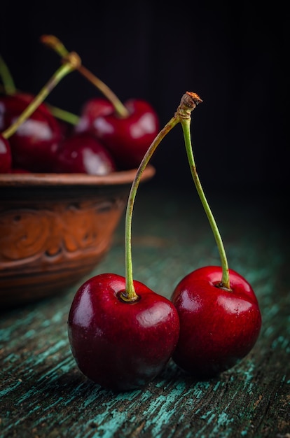 Plato de arcilla con cerezas rojas maduras sobre una mesa de madera vieja.