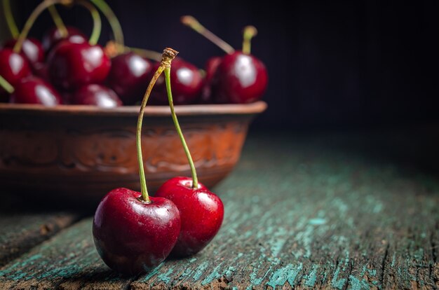 Plato de arcilla con cerezas rojas maduras sobre una mesa de madera vieja.