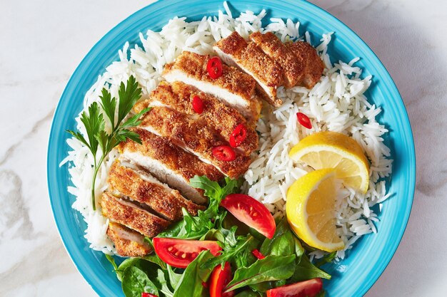 Plato de arroz con chuleta de pollo servido con ensalada de tomate y espinacas, vista horizontal desde arriba, primer plano