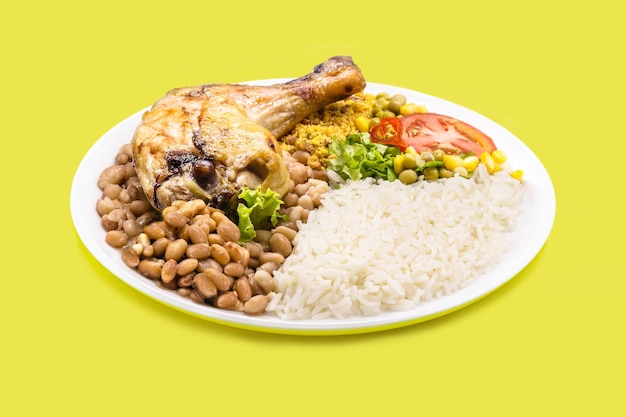 Plato de arroz y frijoles gran muslo de pollo asado ensalada de tomate picado con maíz y guisantes sobre fondo amarillo aislado comida tradicional brasileña