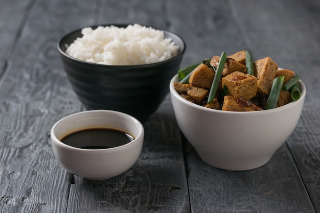 Un plato de arroz y un plato de queso tofu sobre una mesa de madera. Plato asiático vegetariano.