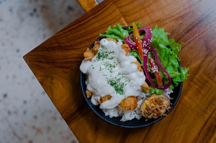Un plato de arroz con pollo con mayonesa de verduras y huevo cocido en la mesa de madera