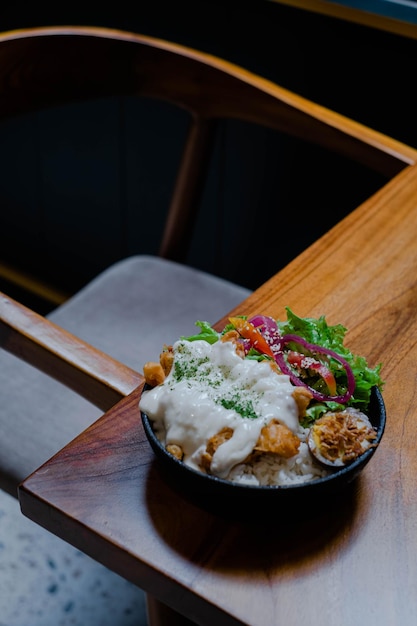 Un plato de arroz con pollo con mayonesa de verduras y huevo cocido en la mesa de madera