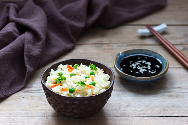 Plato de arroz vegetariano con verduras y guisantes en una superficie de madera