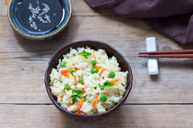 Plato de arroz vegetariano con verduras y guisantes en una superficie de madera