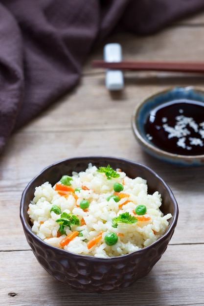 Plato de arroz vegetariano con verduras y guisantes en una superficie de madera