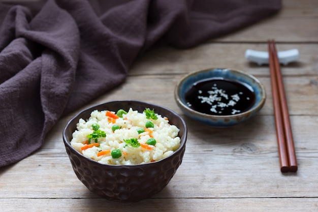 Plato de arroz vegetariano con verduras y guisantes en una superficie de madera