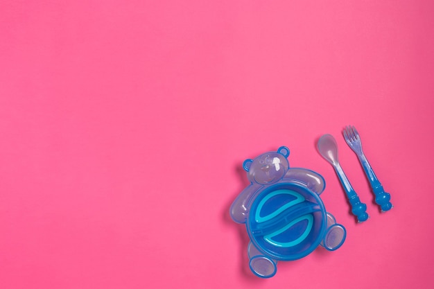 Plato azul bebé con cuchara y tenedor aislado en vista superior rosa