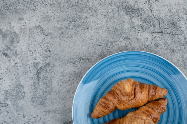 Un plato azul de dos cruasanes recién hechos en una mesa de piedra.