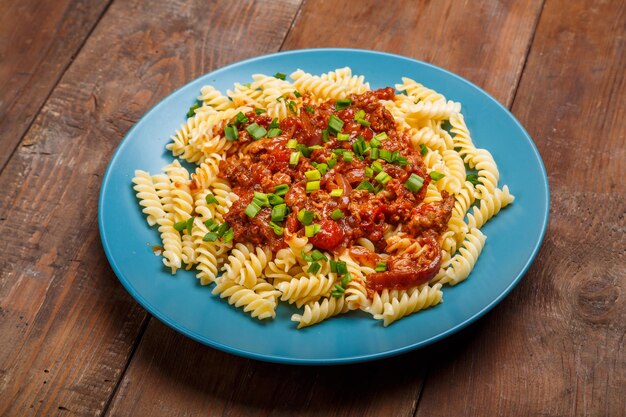 Plato azul con pasta boloñesa sobre una mesa de madera espolvoreada con cebolla