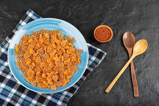 Plato azul de pasta seca sin cocer con especias sobre fondo negro.