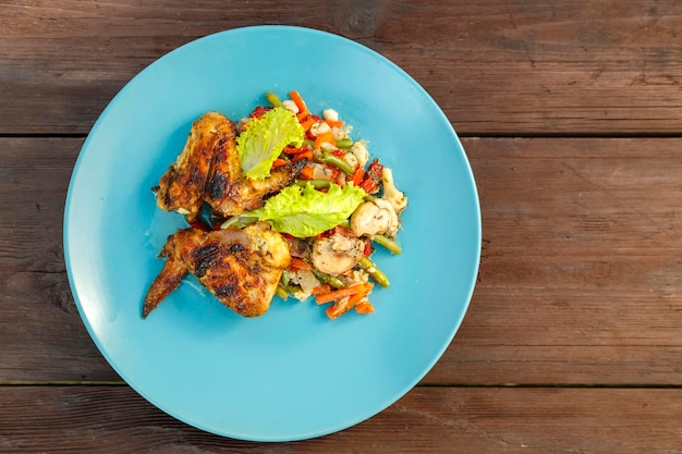 Plato azul con pollo y verduras en una mesa de madera