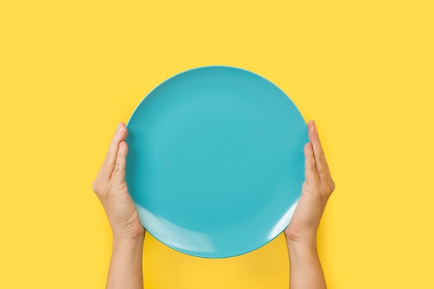 Un plato azul sostenido frente a un fondo amarillo.