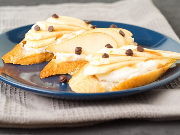 Plato azul con tres tostadas francesas con plátanos, peras, queso crema, gotas de chocolate