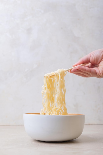 Plato de bambú blanco con fideos de huevo y palillos sobre un fondo claro